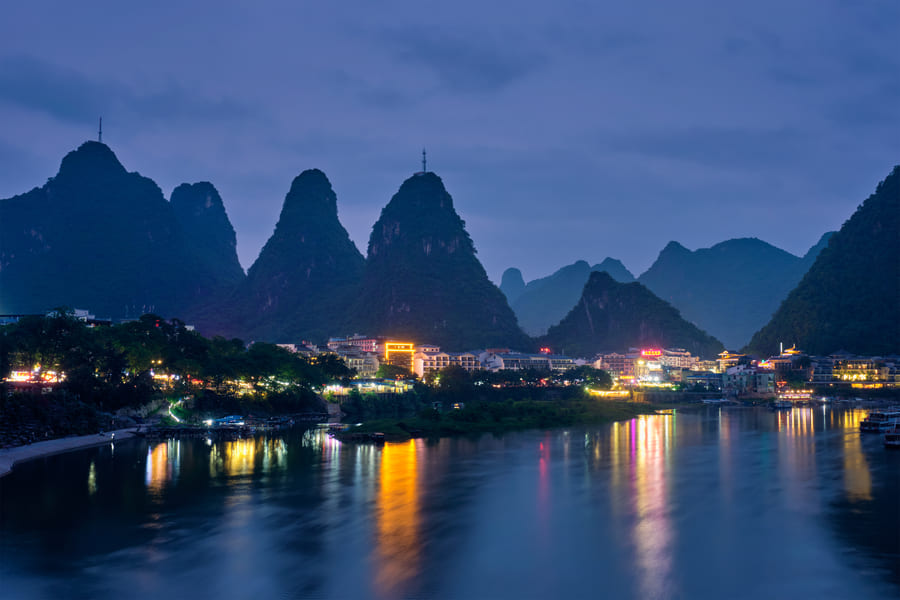 Imagen de montañas imponentes durante la noche y la ciudad en las laderas iluminada tenuemente.