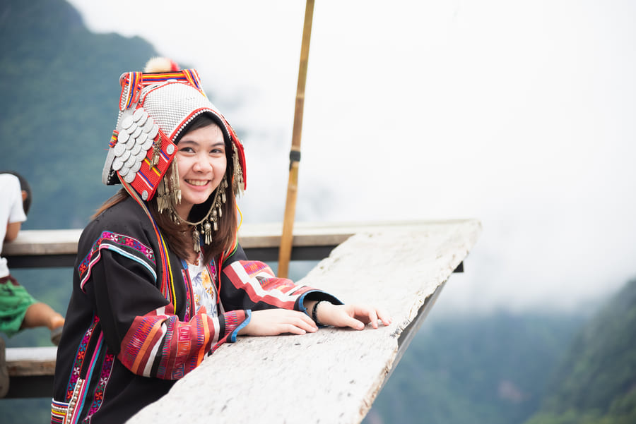 Imagen de una niña con traje típico chino, asomada por un balcon y al fondo montañas con neblina.